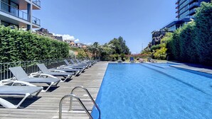 Área ao lado da piscina com espreguiçadeiras e piscina azul cristalina.