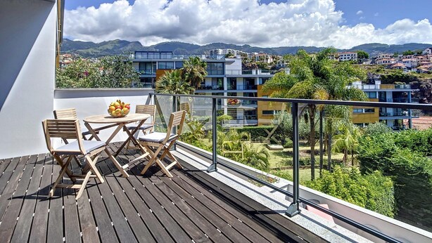 Uma varanda com deck de madeira, uma mesa com cadeiras e uma fruteira.