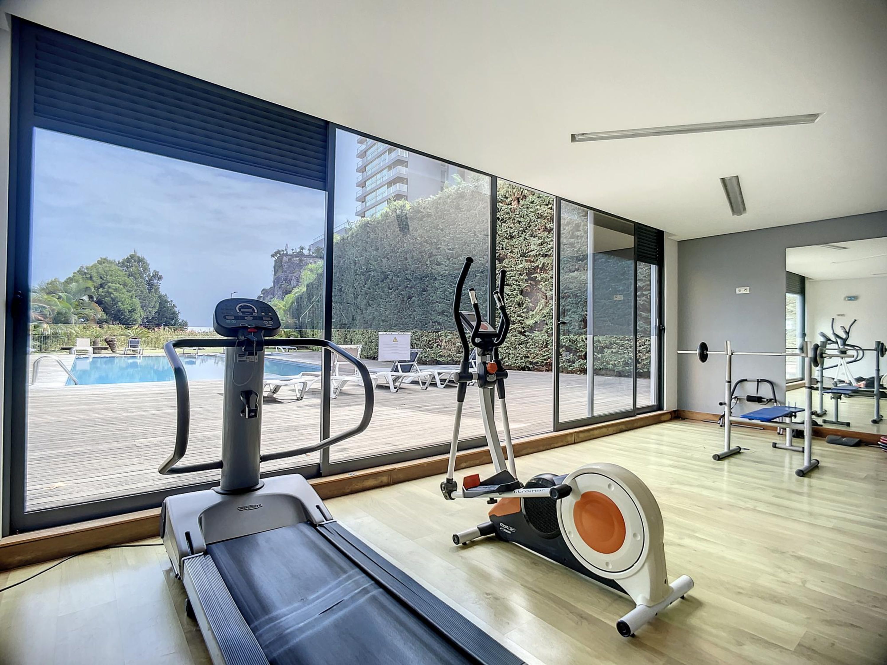 A gym with a treadmill, elliptical, and rowing machine, overlooking a pool and outdoor area.