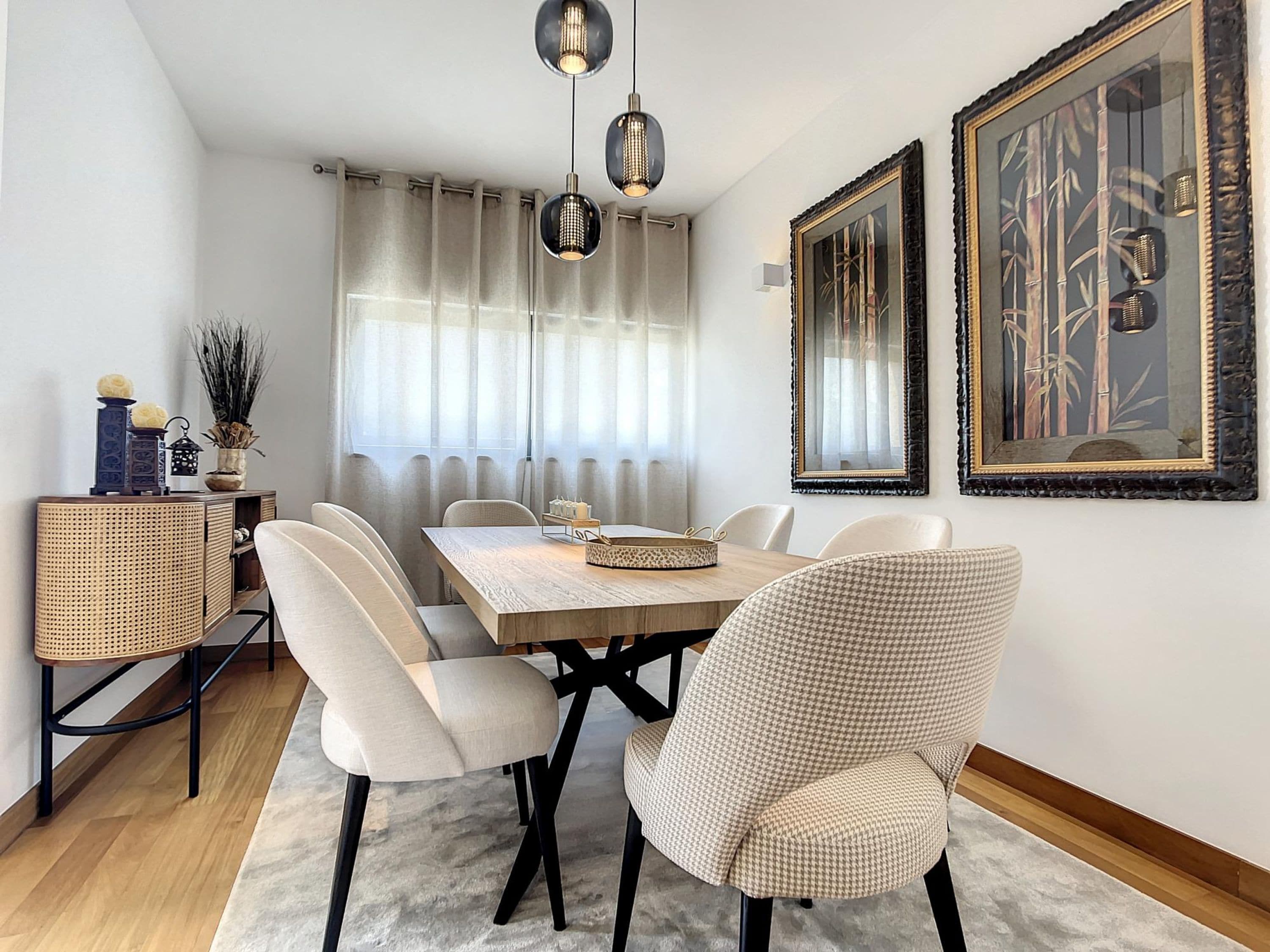 A dining area with a wooden table, white chairs, a woven side table, and two hanging pendant lights.