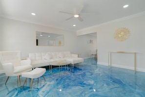 A room with a white sofa set, a glass coffee table, and a ceiling fan.