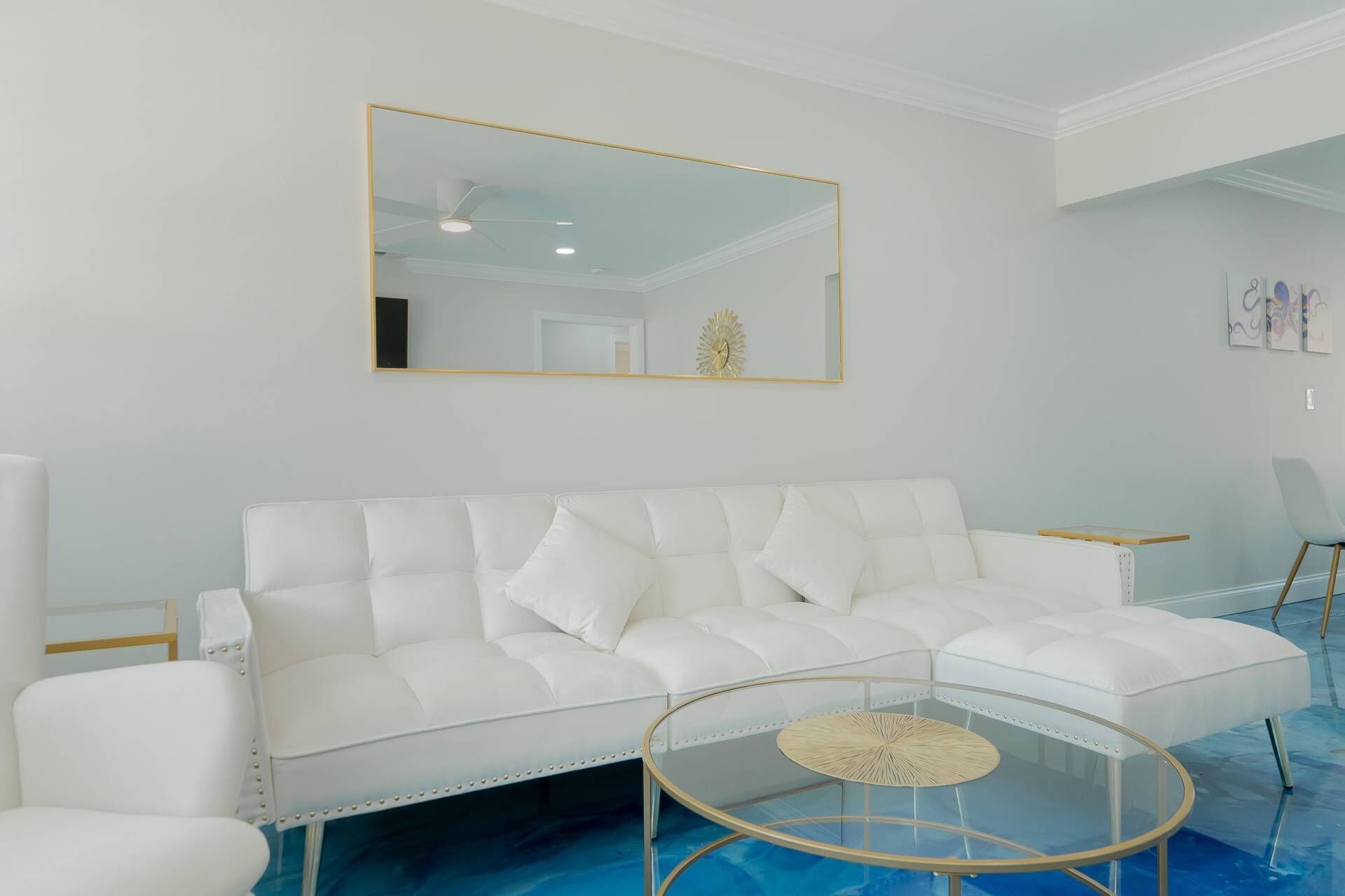 A white leather sofa with a glass coffee table in a modern room with a large mirror and minimal decor.