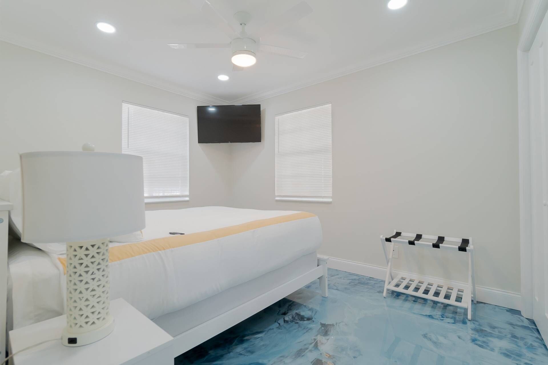 A bedroom with a bed, a TV mounted on the wall, and a ceiling fan.