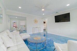 Een moderne woonkamer met een witte bank, een glazen salontafel en een plafondventilator.
