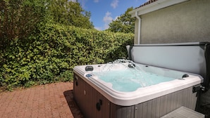 Ein Whirlpool mit Holzterrasse und einem kleinen Tisch daneben, umgeben von üppigem Grün.