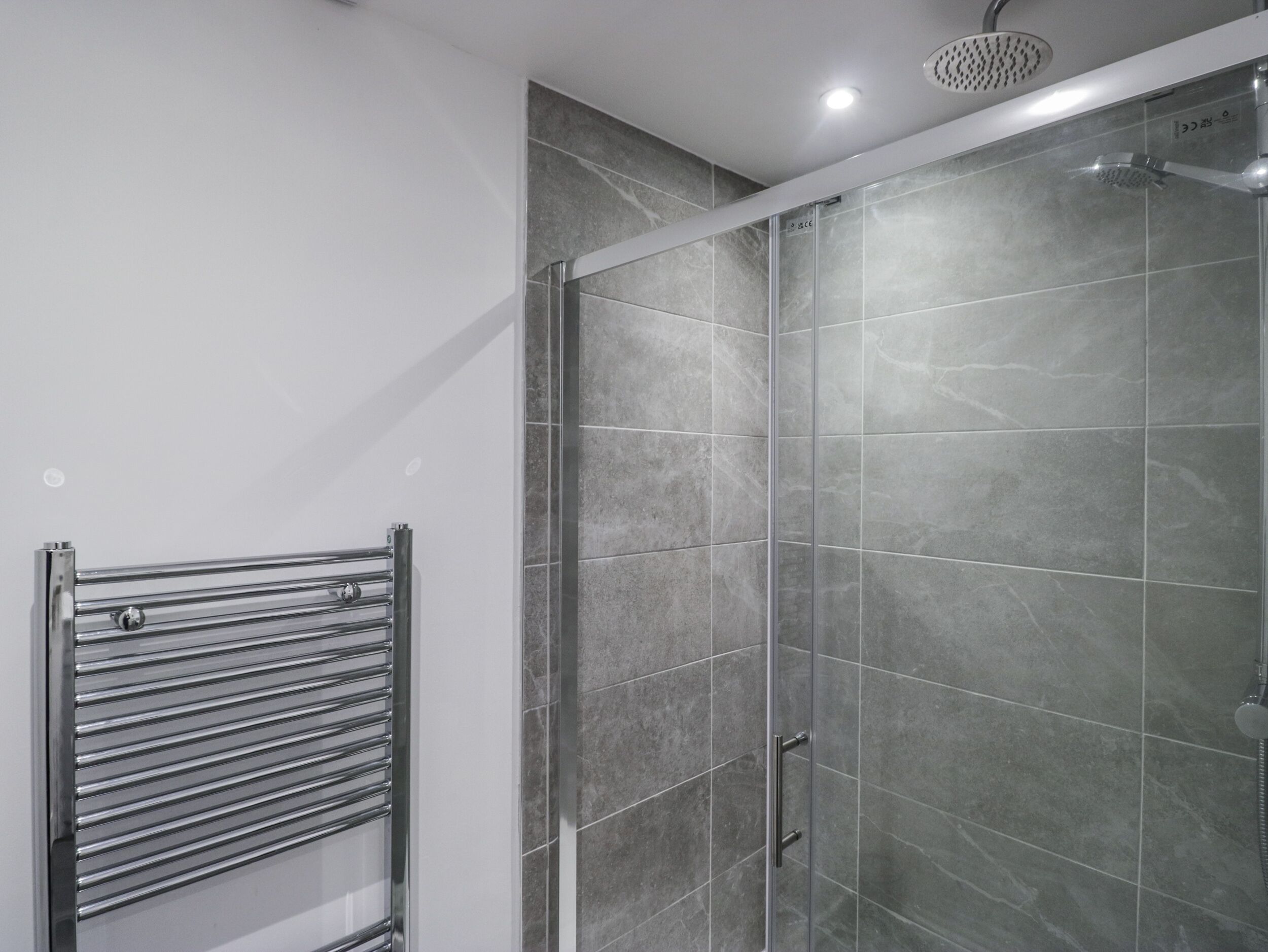 A modern bathroom with a glass shower enclosure, a chrome towel rack, and grey marble tiles.