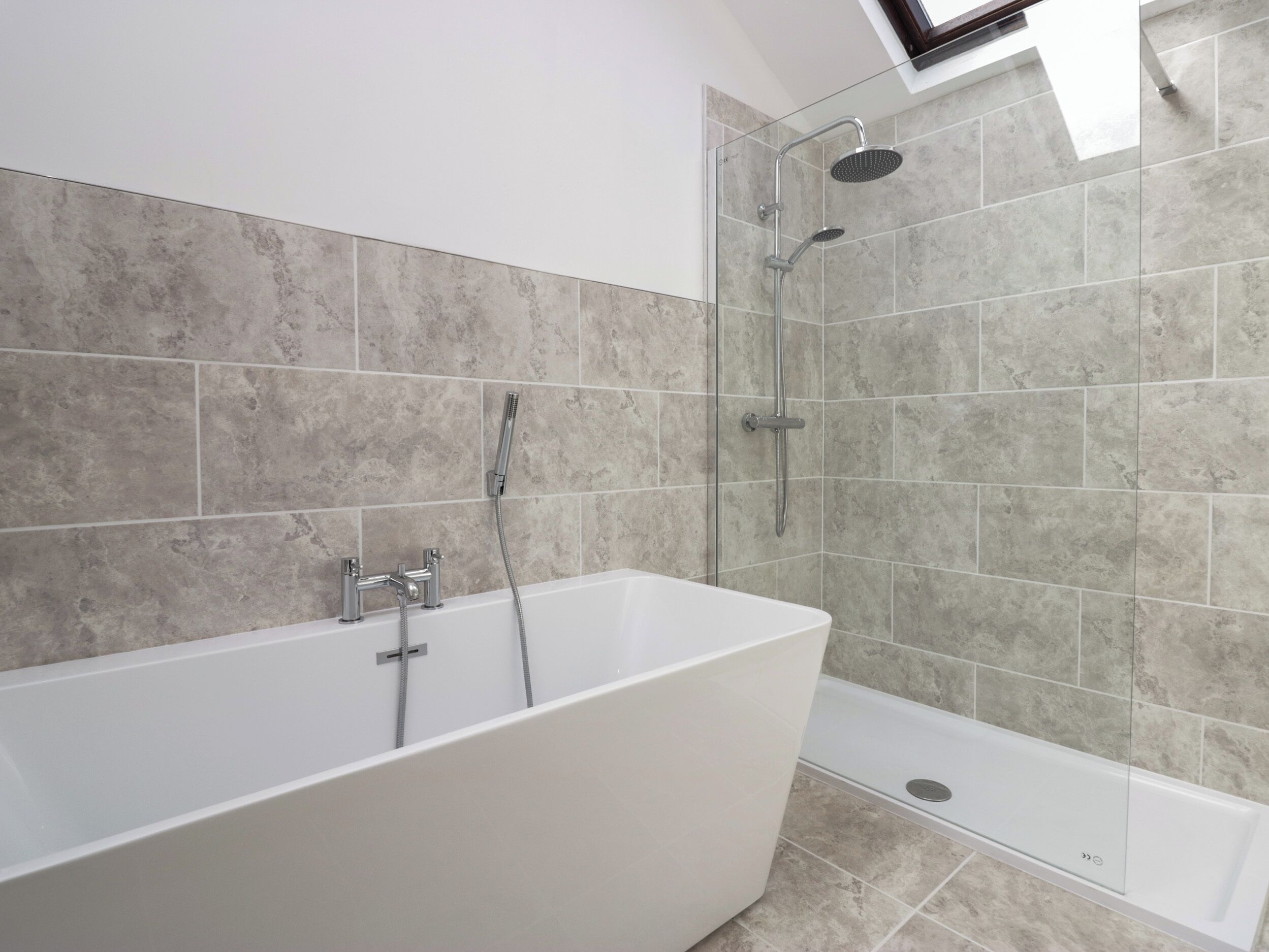 A modern bathroom with a freestanding bathtub, a glass-enclosed shower, and a skylight above.