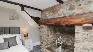 A bedroom with a stone fireplace, a bed with white bedding, a nightstand, and a lamp.
