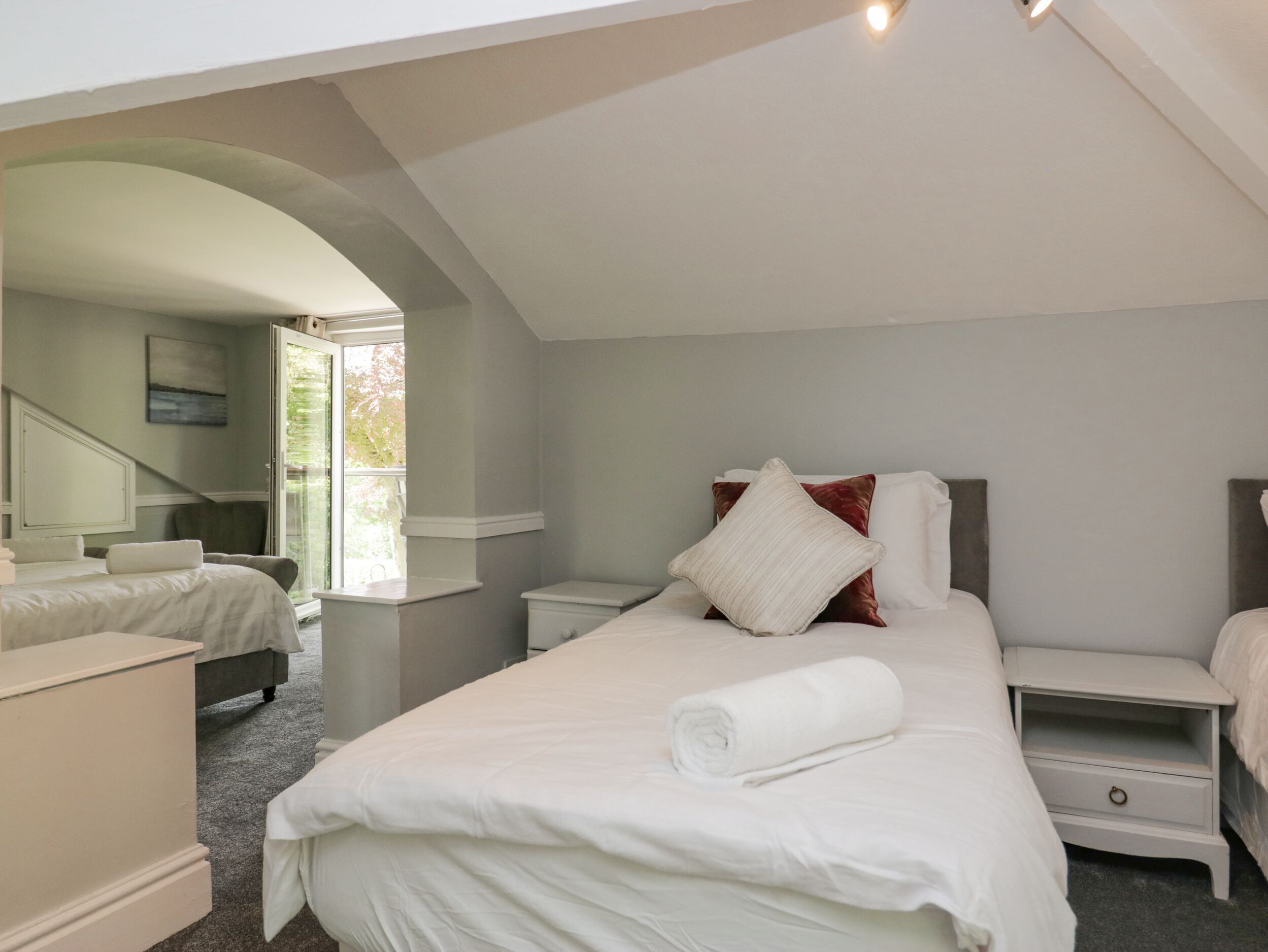 A bedroom with a large bed, a nightstand, a dresser, and a window with a view.