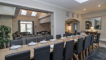 Uma sala de jantar ampla, com uma mesa comprida posta para refeição, rodeada por assentos confortáveis.