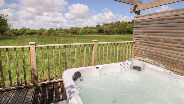 Ein Whirlpool auf einer Holzterrasse mit Blick auf ein Wiesenfeld und Bäume.