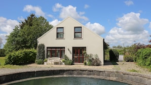 Ein zweistöckiges Haus mit einer Veranda, einem kleinen Garten und einem Teich davor.