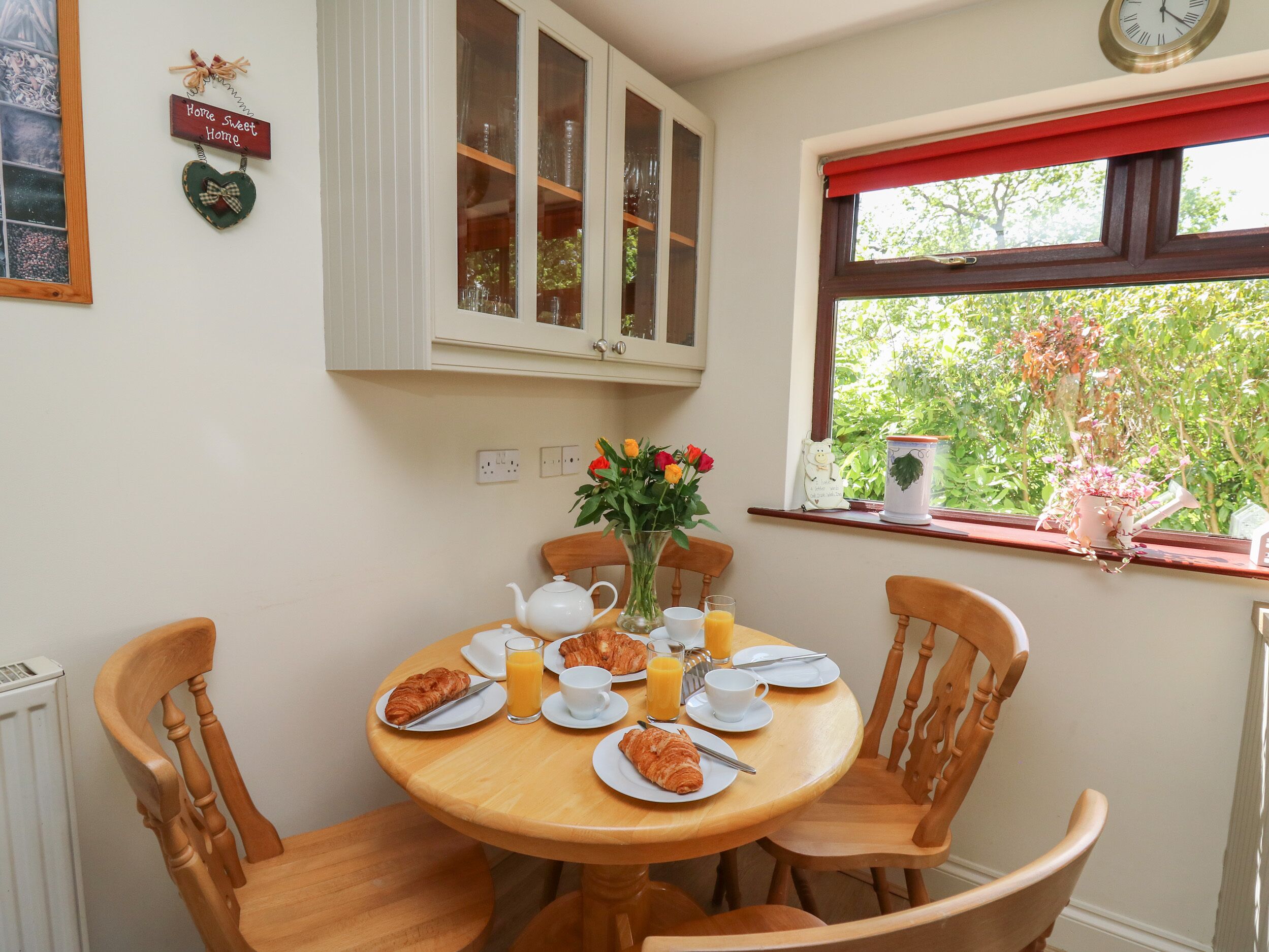 Un comedor con una mesa redonda de madera dispuesta para el desayuno, incluyendo croissants, jugo y un florero con flores.