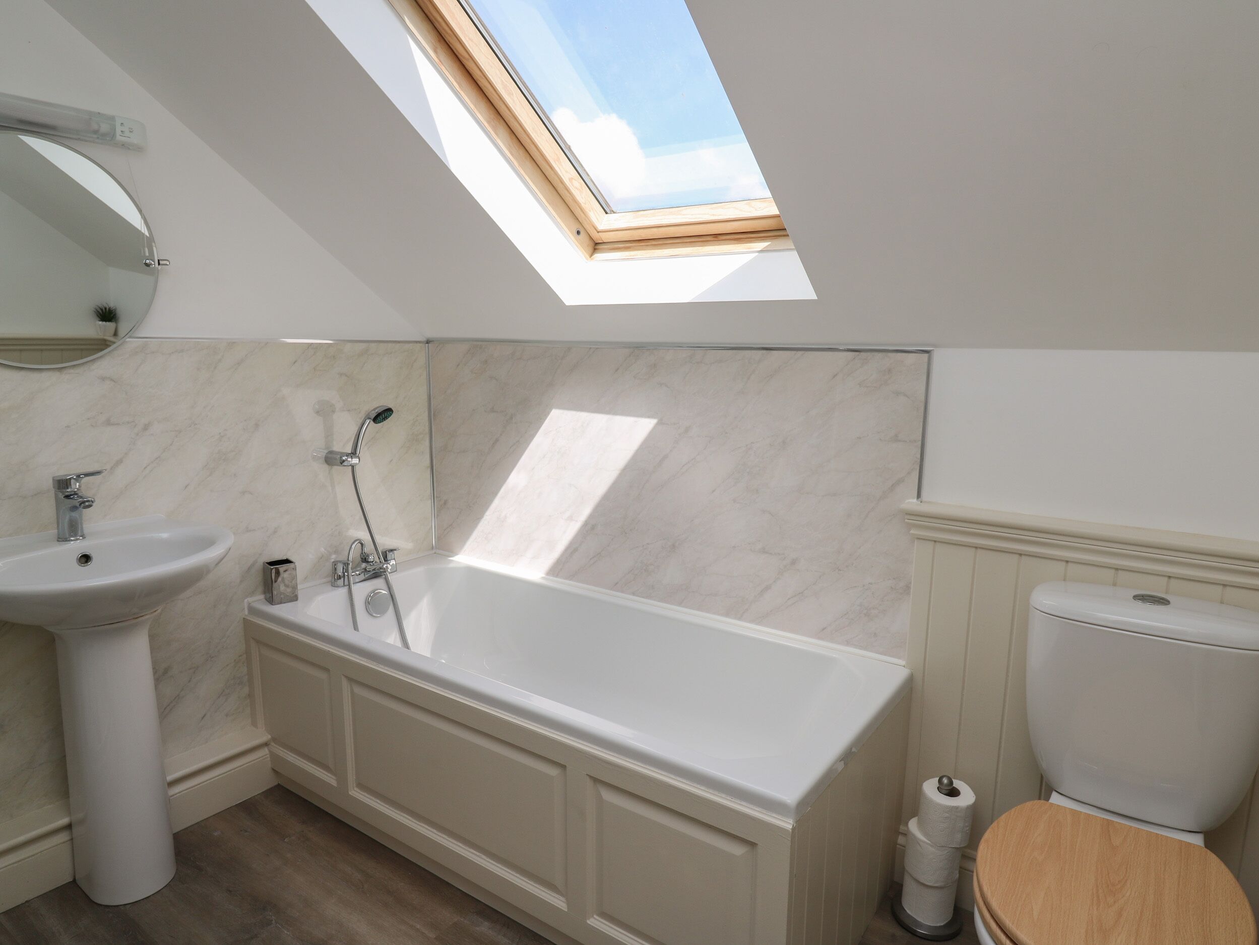A modern bathroom with a skylight, a freestanding bathtub, a pedestal sink, and a toilet.