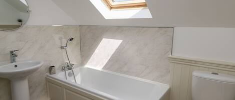 Ein modernes Badezimmer mit Dachfenster, einer freistehenden Badewanne, einem Standwaschbecken und einer Toilette.
