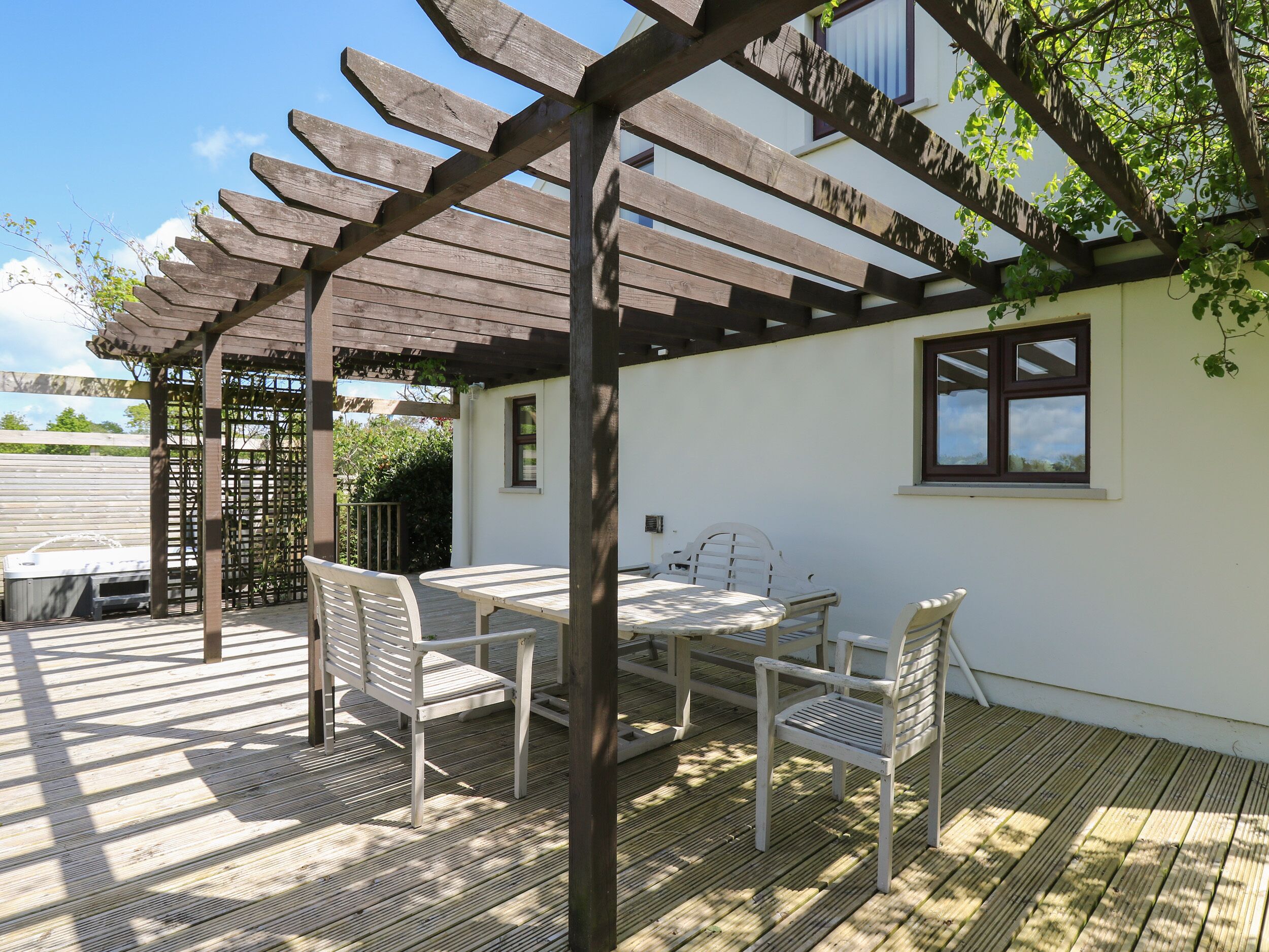 A covered patio area with a wooden pergola, a table, and two chairs.