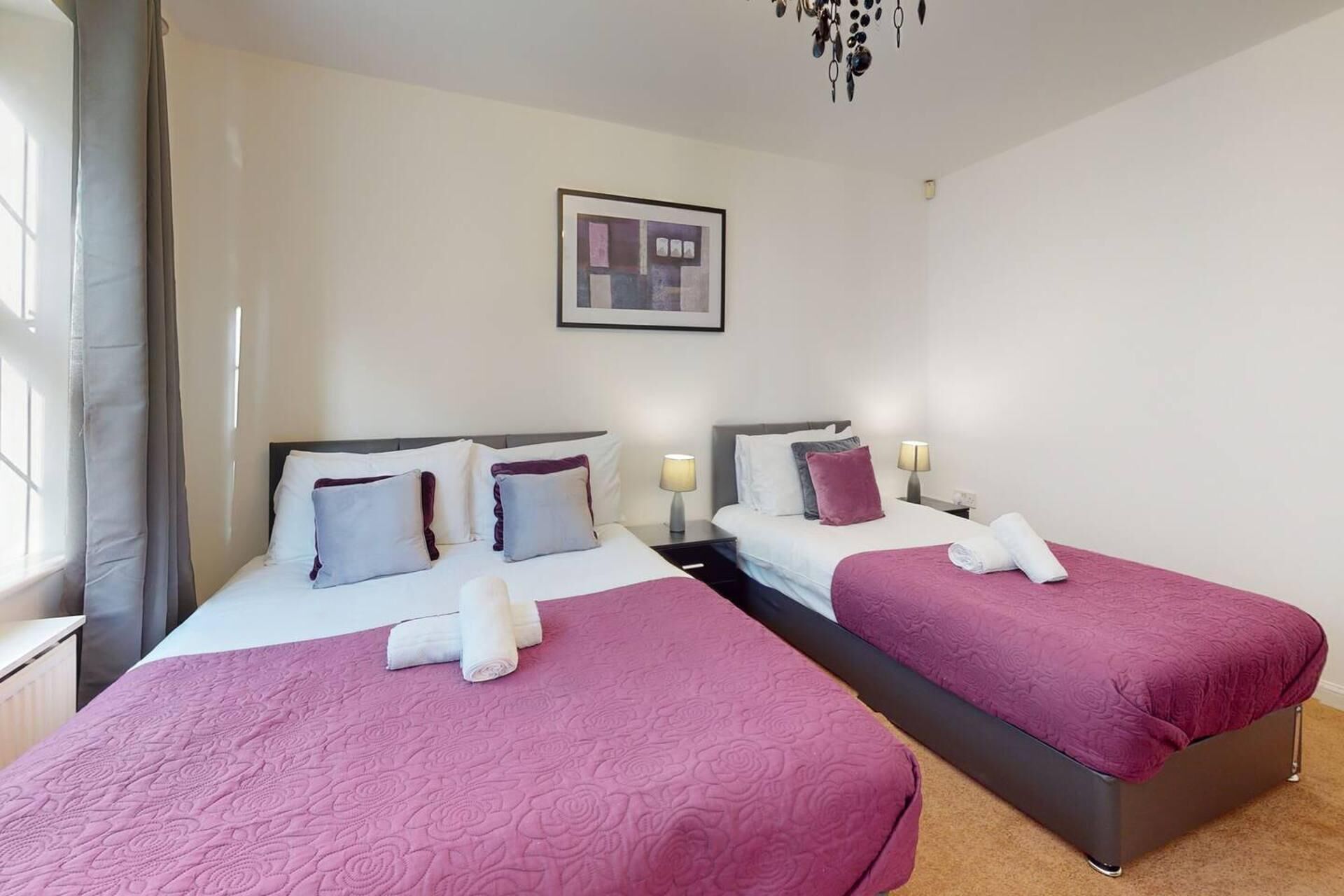 A hotel room with two beds, each with a pink bedspread and white pillows. There is a framed picture on the wall above the beds.