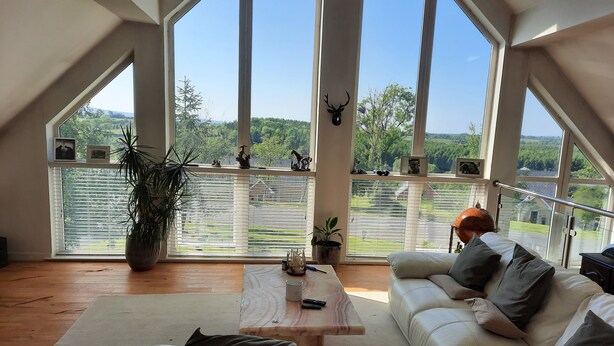 Ein geräumiger Raum mit großem Fenster, einem weißen Sofa, einem Holztisch und einem Blumentopf.