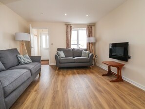 Ein Wohnzimmer mit grauem Sofa, einem Holztisch und einem an der Wand montierten Flachbildfernseher.