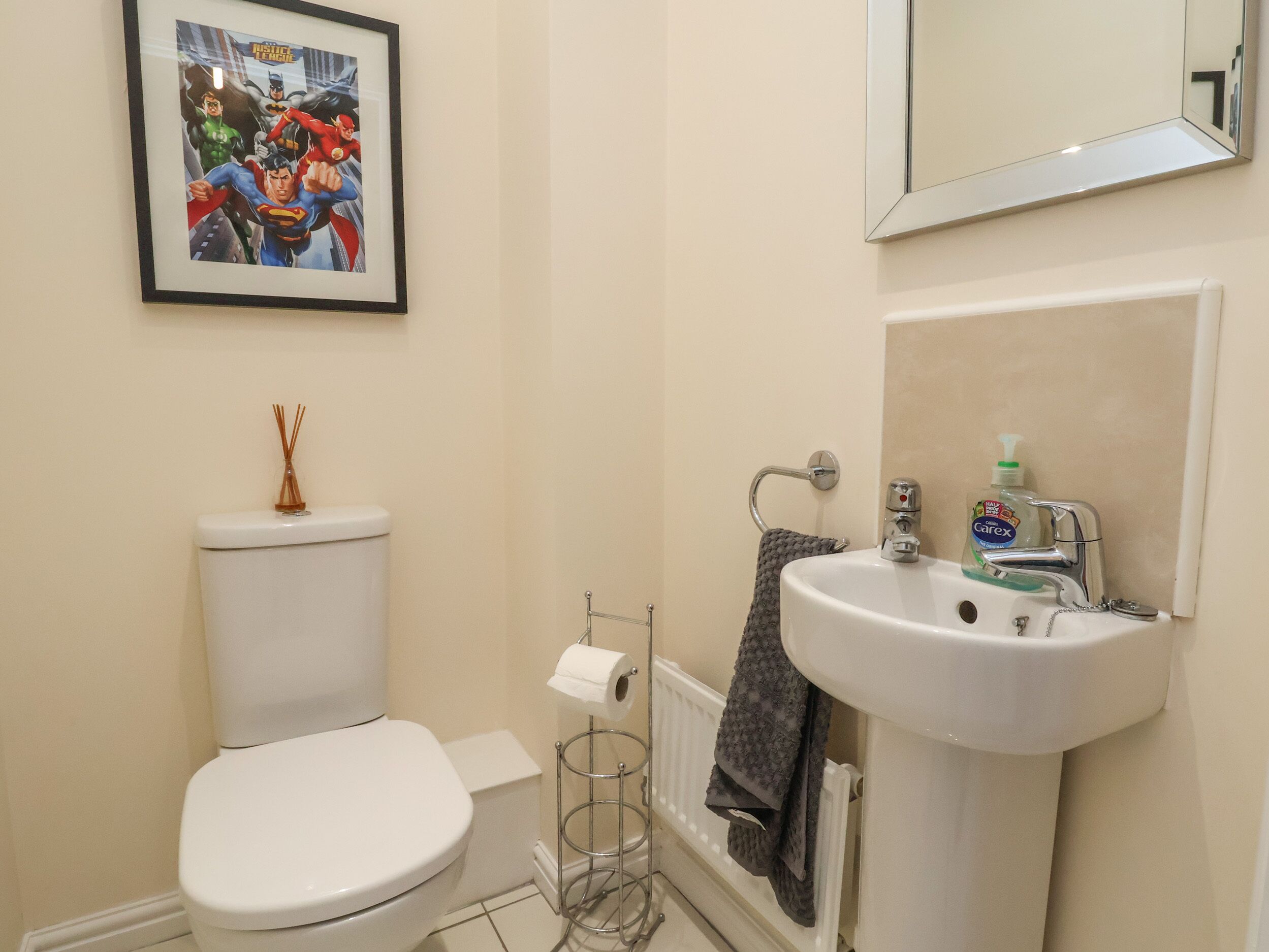 A bathroom with a toilet, a sink, a mirror, and a framed superhero comic on the wall.