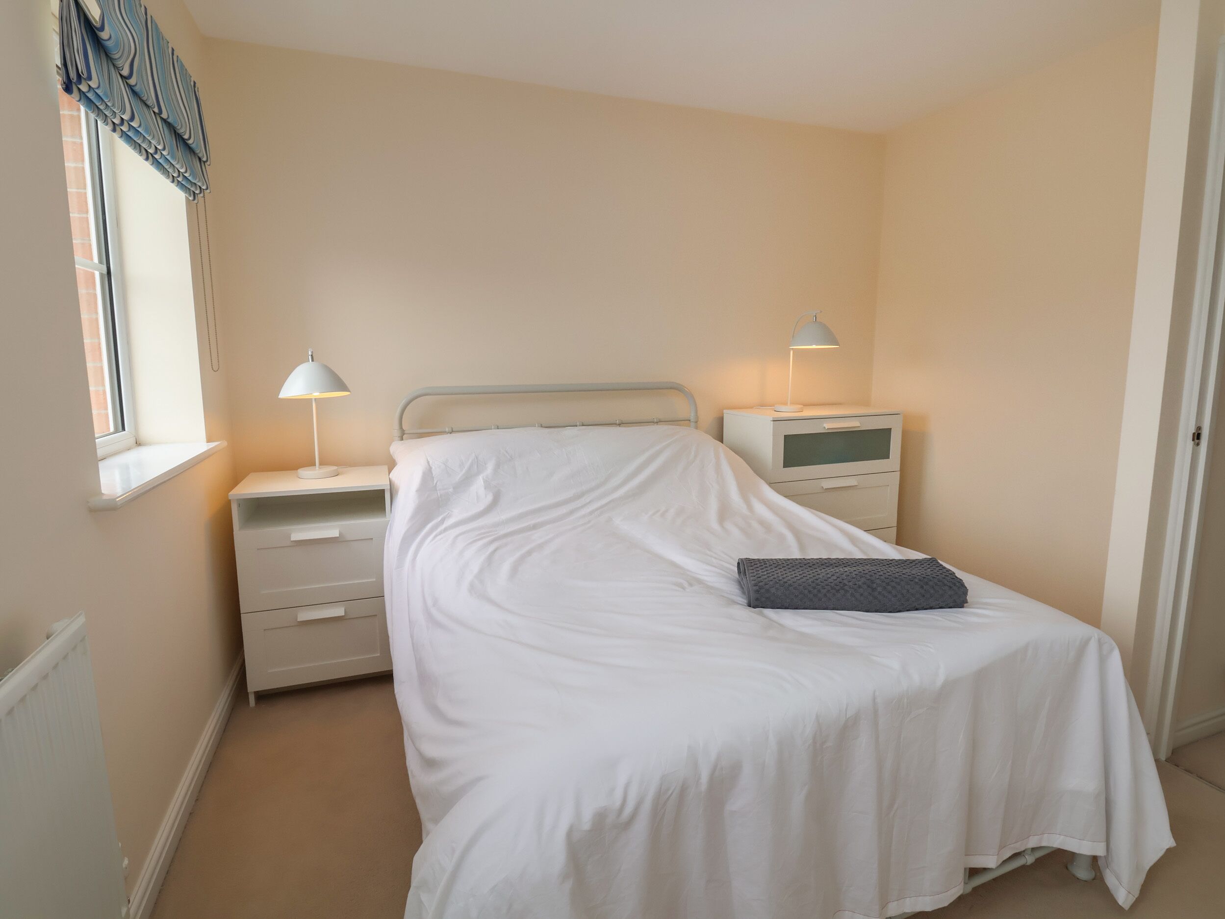 Un dormitorio ordenado con una cama individual, mesitas de noche y una ventana con cortinas.