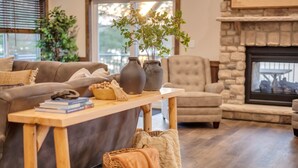 A cozy living room with a fireplace, a sofa, a coffee table, and a bookshelf. - Lake Front Livin by PMR, 8BR Lakefront, Private Beach & Dock, Sleeps 26 (Lake Harmony)