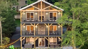 A two-story house with a balcony, a dock, and a pond. - Lake Front Livin by PMR, 8BR Lakefront, Private Beach & Dock, Sleeps 26 (Lake Harmony)