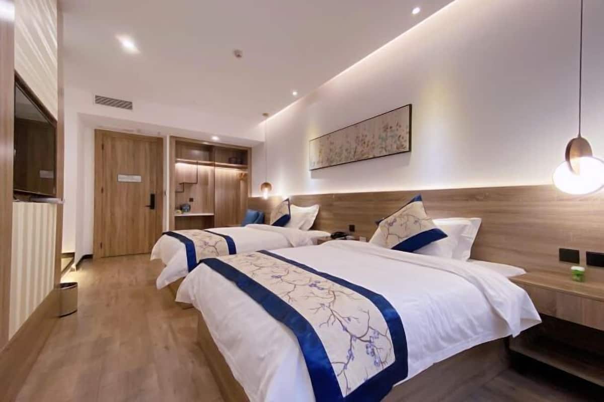 A modern hotel room with two beds, wooden flooring, a large window, and a wall-mounted artwork.