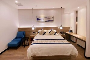 A hotel room with a bed, a blue chair, a nightstand, and a painting on the wall. - Flower Seasons Hotel (Dafang)