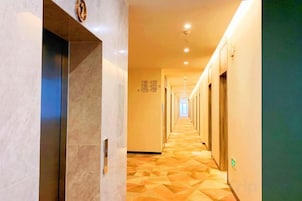 Un pasillo de hotel con una pared de mármol a la izquierda, suelo de madera y una serie de puertas a la derecha.