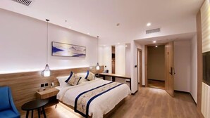 A modern hotel room with a wooden floor, a bed with a blue and white bedspread, a bedside table with a lamp, and a painting on the wall. - Flower Seasons Hotel (Dafang)