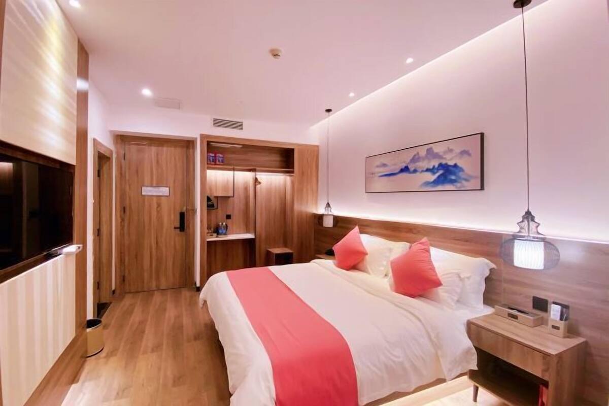 A hotel room with a bed, bedside table, nightstand, and a painting on the wall.