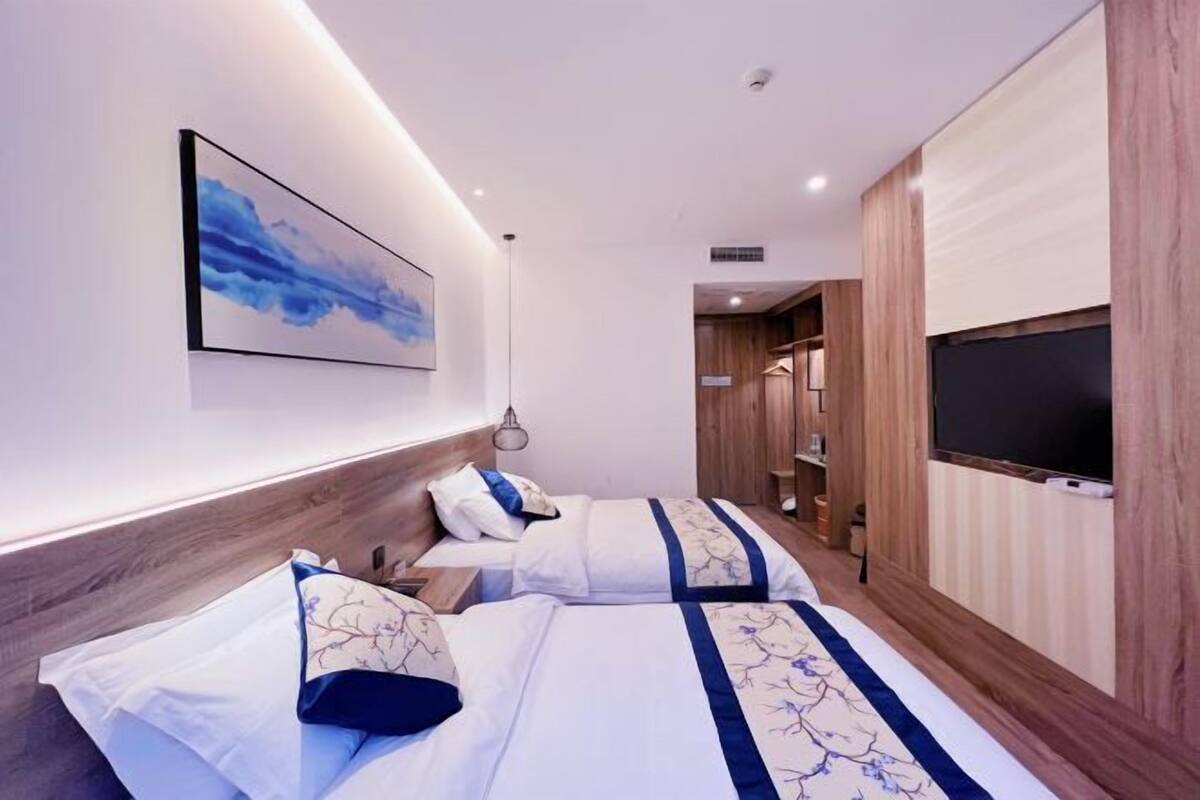 A hotel room with two beds, a flat-screen TV, a painting on the wall, and a wooden headboard.