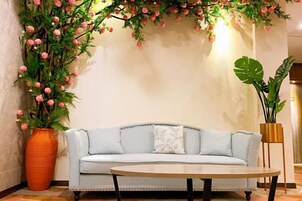 Una habitación con un sofá azul claro, una mesa redonda de madera y una planta grande en maceta con flores rosas.