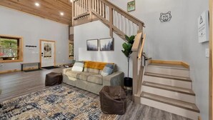 Un salon spacieux avec un escalier en bois, un canapé, une table basse et un tapis à motifs.