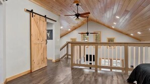 Une chambre spacieuse située dans les combles, avec un plafond en bois, un ventilateur de plafond et une grande porte coulissante de style grange.