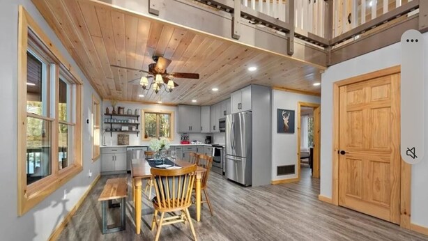 Une cuisine spacieuse avec un plancher en bois, un coin repas avec une table et des chaises en bois, et un ventilateur de plafond.