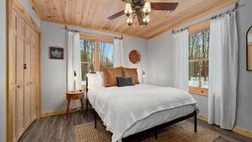 A bedroom with a wooden ceiling, a bed with white bedding, a nightstand, and a window with curtains.