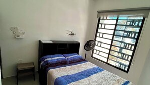 A bedroom with a bed, a nightstand, a ceiling fan, a window with bars, and a wall-mounted light fixture.