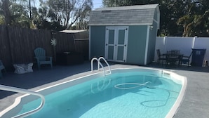 A rectangular swimming pool with a white edge, a ladder, and a hose. There is a small shed with a door and windows in the background. - Pool spacious home in the heart of town (St. Petersburg)