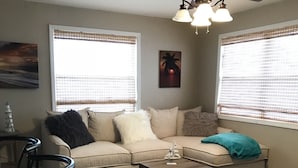 A living room with a sectional sofa, a coffee table, and a dining area with chairs. There are windows with blinds, a painting on the wall, and a ceiling light fixture. - Pool spacious home in the heart of town (St. Petersburg)