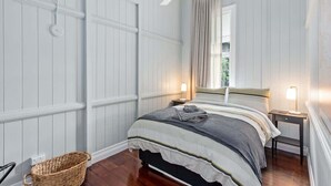 A bedroom with a bed, a ceiling fan, a nightstand, a lamp, and a wicker basket.
