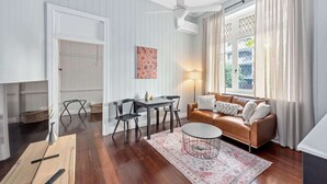 A room with a white ceiling fan, a brown leather sofa, a dining table with chairs, and a patterned rug.