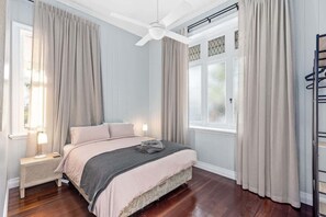 Une chambre à coucher avec un lit, un ventilateur de plafond, une table de chevet et une fenêtre avec des rideaux.