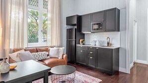 A modern kitchen with dark cabinets, a microwave, and a sink. There is a brown leather sofa with cushions and a small round table with a vase.