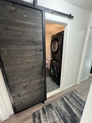 Une buanderie équipée d’un lave-linge et d’un sèche-linge, avec une porte coulissante en bois et un tapis à carreaux.