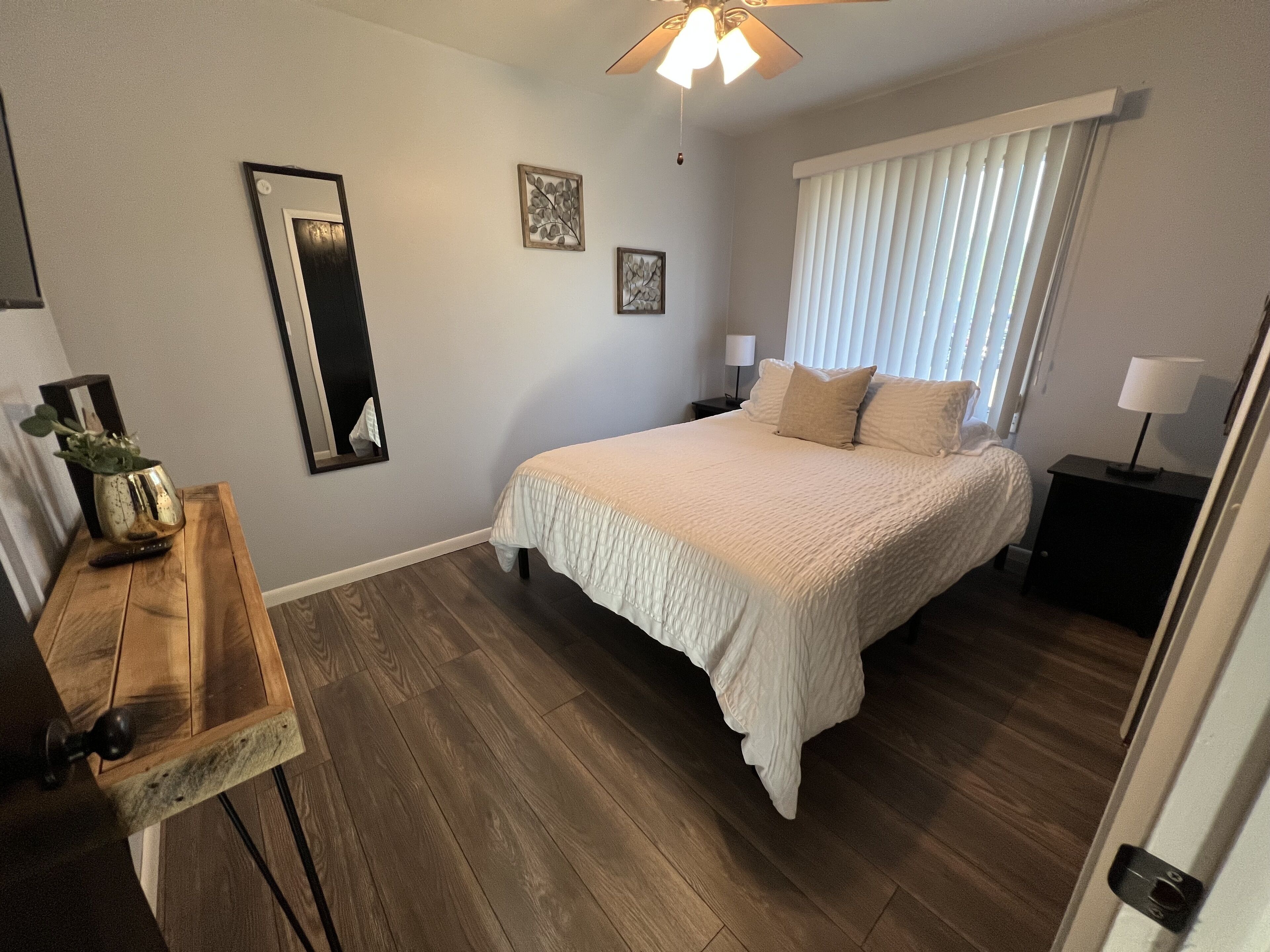 A bedroom with a bed, bedside tables, a mirror, and a ceiling fan.