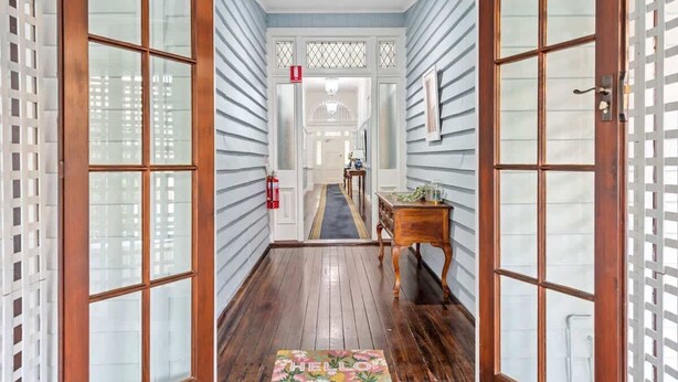 A hallway with wooden flooring, a welcome mat, and a door leading to a room.