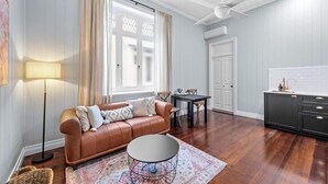 A living room with a leather sofa, a round coffee table, a dining table, and a kitchen area with a black cabinet.