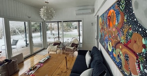 A spacious living area with a large window, a wooden coffee table, a dark sofa, and a colorful abstract painting on the wall.